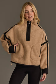 A woman models the Panache Apparel Collection Tan & Black Half Zip Sherpa Fleece Sweatshirt, featuring black accents and a zipper, as she stands against a gray background with one hand in her pocket and a relaxed expression.