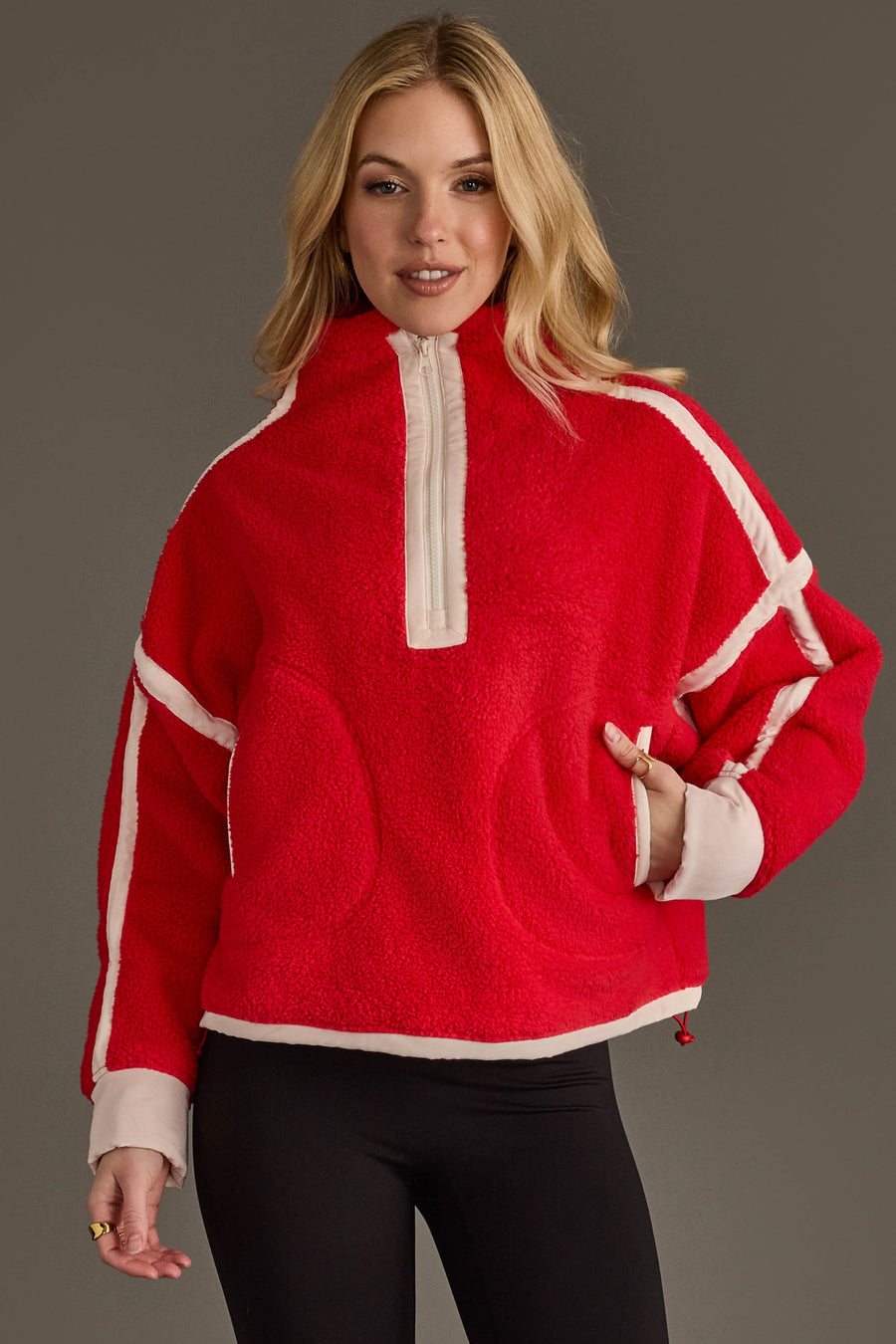 A woman wearing the Panache Apparel Collection Red & Beige Half Zip Sherpa Fleece Sweatshirt with white trim and zipper, paired with black leggings, stands against a gray background with one hand in the pocket.