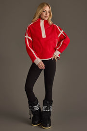 A woman models the Panache Apparel Collection’s Red & Beige Half Zip Sherpa Fleece Sweatshirt, paired with black leggings and black snow boots. She stands against a plain gray background with one hand on her hip, looking at the camera.