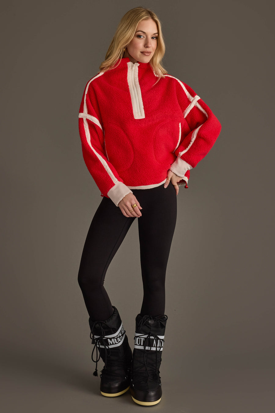 A woman models the Panache Apparel Collection’s Red & Beige Half Zip Sherpa Fleece Sweatshirt, paired with black leggings and black snow boots. She stands against a plain gray background with one hand on her hip, looking at the camera.