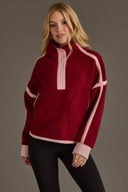 A woman wearing the Panache Apparel Collection Burgundy & Light Pink Half Zip Sherpa Fleece Sweatshirt and black leggings stands against a plain gray background, looking at the camera and smiling slightly.
