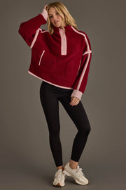A woman poses in the Panache Apparel Collection Burgundy & Light Pink Half Zip Sherpa Fleece Sweatshirt, paired with black leggings and white sneakers, against a plain gray background.