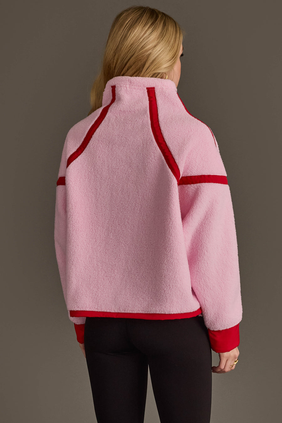 A person with long blonde hair, facing away from the camera against a plain gray background, wears the Panache Apparel Collection Light Pink & Red Half Zip Sherpa Fleece Sweatshirt paired with black pants.