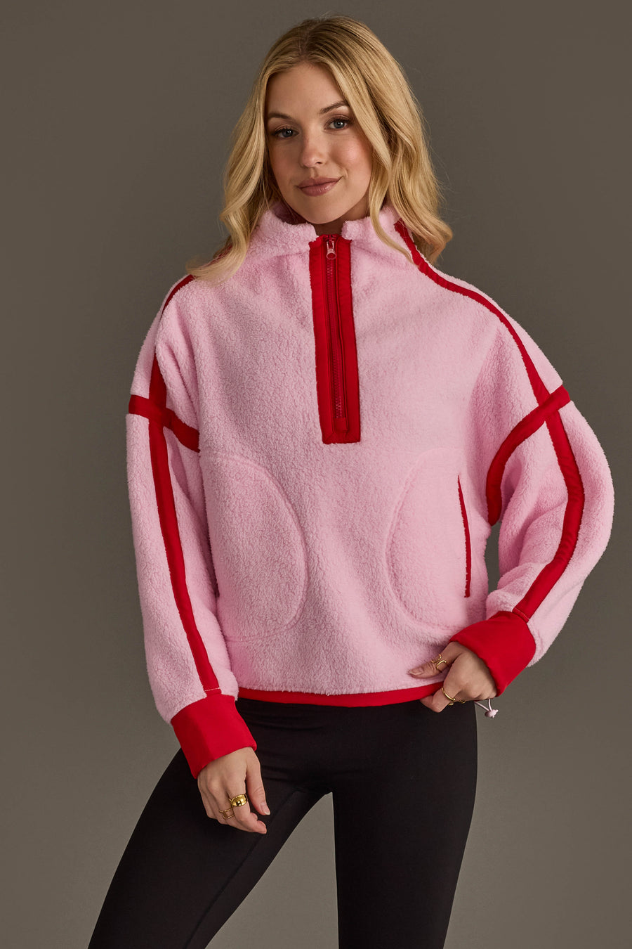 A woman stands against a plain gray background, smiling slightly with one hand on her hip, wearing the Panache Apparel Collection Light Pink & Red Half Zip Sherpa Fleece Sweatshirt.