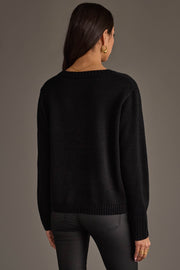 A woman with long brown hair, wearing gold hoop earrings and black pants, stands facing away against a plain dark background, modeling the Drink At The Game Sweater by Panache Apparel Collection.
