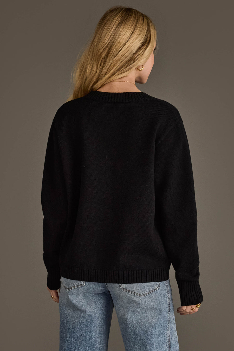 A person with long blonde hair, seen from behind against a plain brown background, is wearing the Panache Apparel Collection's "It's A Good Day For Football" soft sweater in black paired with blue jeans.