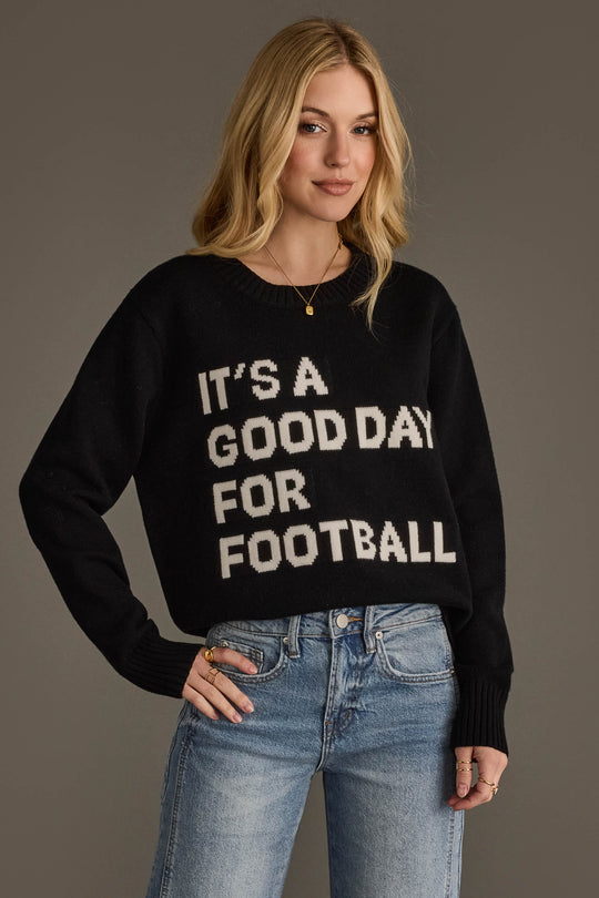 A woman with long blonde hair wears the Panache Apparel Collection It's A Good Day For Football Soft Sweater in black, paired with blue jeans, as she stands against a plain background.