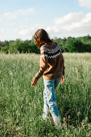 Back lifestyle view of Panache Apparel’s brown Fair Isle sweater styled with light wash jeans and white western boots.