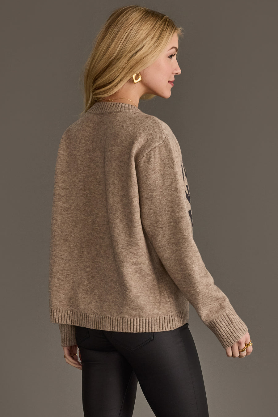 A woman viewed from the side wearing a taupe long-sleeved Taupe Holiday In The Mountains Soft Sweater with a crew neck and ribbed cuffs.
