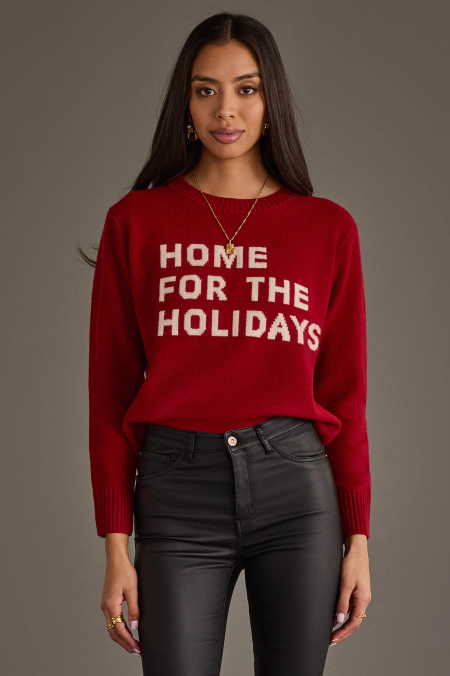 A person wearing a red Home For The Holidays Soft Sweater with white text, paired with black pants.