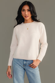 A woman models the Panache Apparel Collection Cream Soft Sweater, paired with blue jeans and gold jewelry. She stands against a plain gray background, looking at the camera in a relaxed pose.