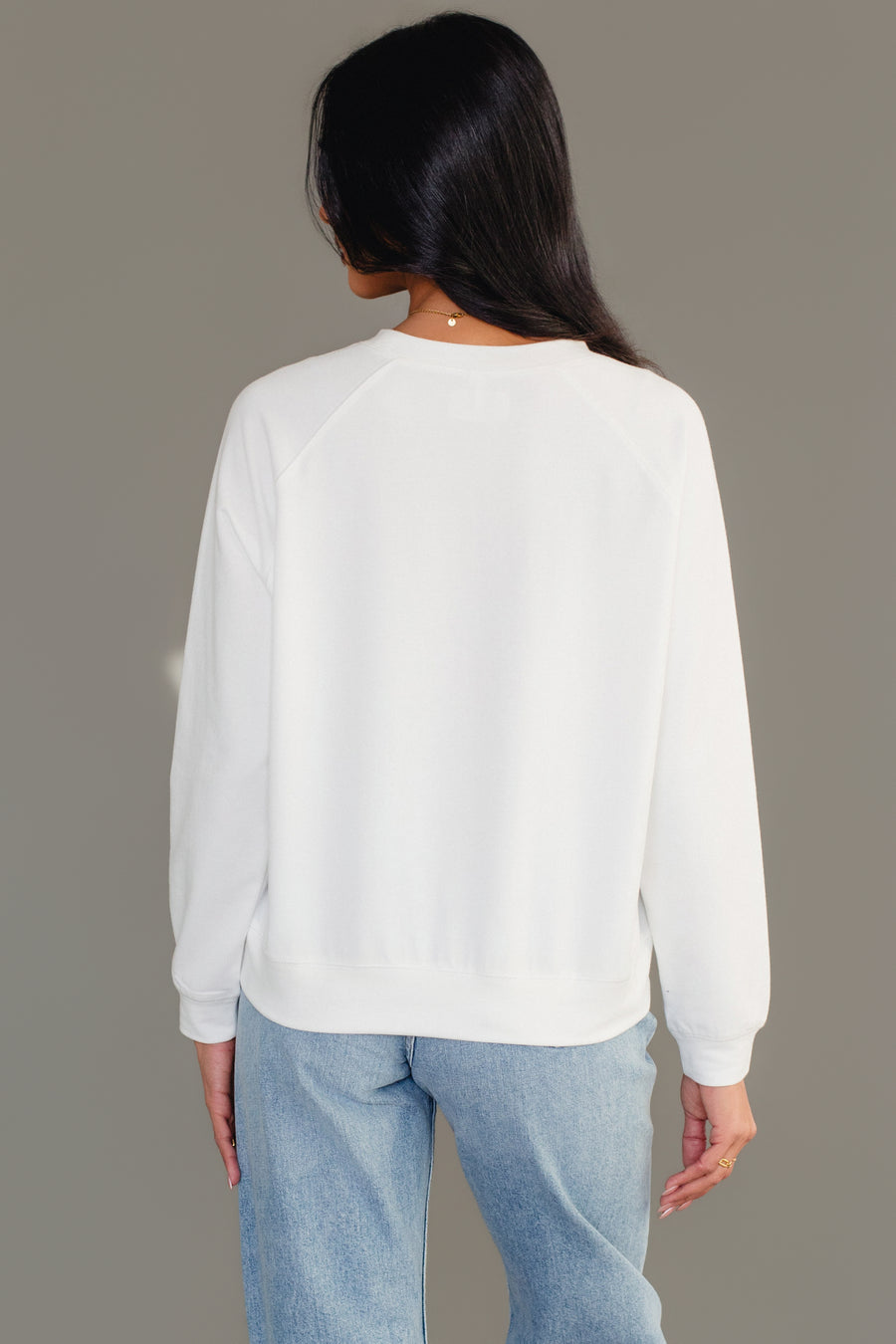 Back view of a person wearing a plain white crewneck Merry Bar Cart Sweatshirt and blue jeans.
