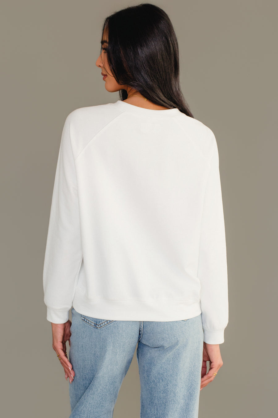 A person seen from the back wearing a Girl With Christmas Tree Sweatshirt in plain white and blue jeans.