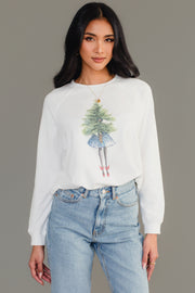 A person wearing a white long-sleeve Girl With Christmas Tree Sweatshirt featuring an illustration of a figure carrying a Christmas tree on the front.