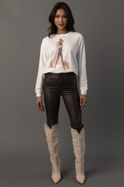 A woman stands against a plain background wearing the Panache Apparel Collection’s “Girl At Pumpkin Patch” sweatshirt, paired with black leather pants and light-colored knee-high cowboy boots.