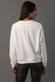 A woman with long brown hair is standing and facing away, wearing the Panache Apparel Collection “Girl Walking Turkeys” white long-sleeve sweatshirt paired with black pants, against a plain gray background.