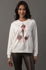 A woman models the Panache Apparel Collection’s “Girl Walking Turkeys Sweatshirt”—a white top featuring an illustration of a stylish girl walking two turkeys amid red leaves—paired with dark pants and set against a gray background.