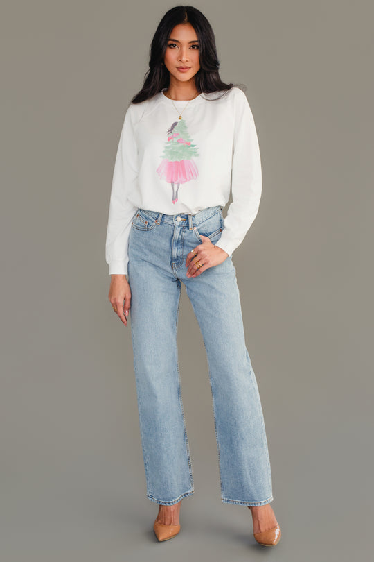 A Panache Apparel Collection Pink Girl Holding Tree Sweatshirt in white, featuring a girl in a pink skirt standing in front of a green tree, worn with light-wash blue jeans and tan heels.