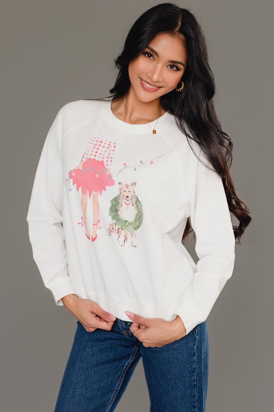 A woman wearing a white Christmas Girl & Dog Sweatshirt featuring a watercolor illustration of a girl holding a gift and a dog wearing a wreath.