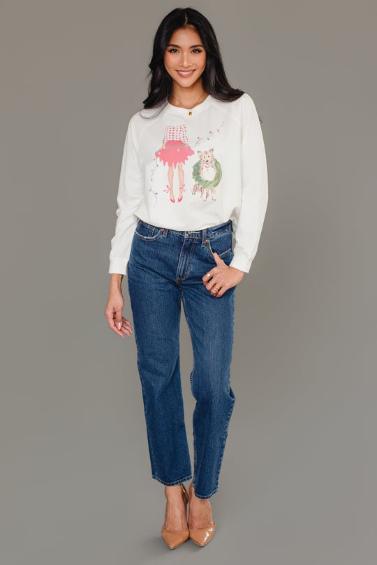 A woman wearing a white Panache Apparel Collection Christmas Girl & Dog Sweatshirt, paired with blue jeans and tan heels.