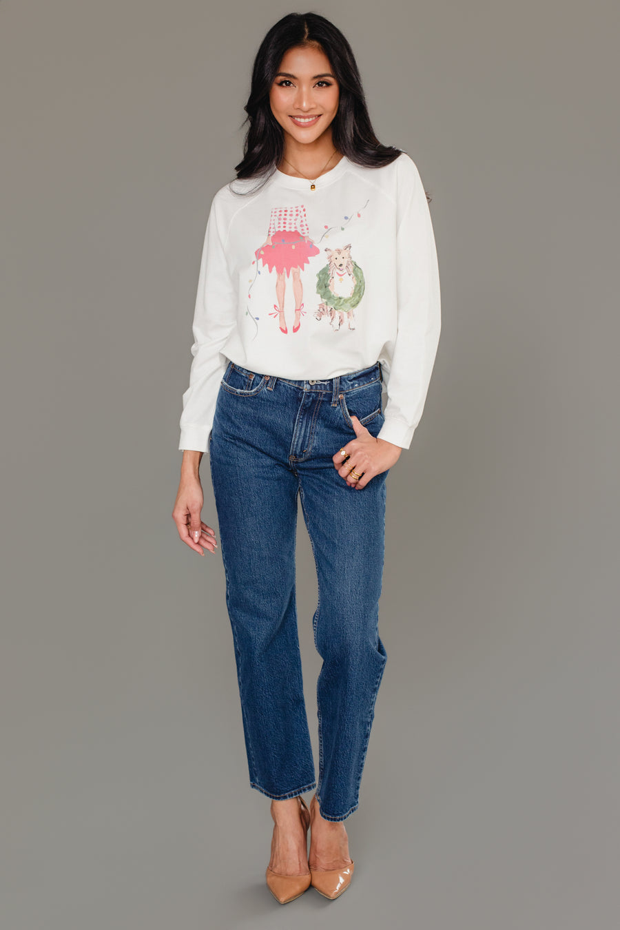 A woman wearing a white Panache Apparel Collection Christmas Girl & Dog Sweatshirt, paired with blue jeans and tan heels.