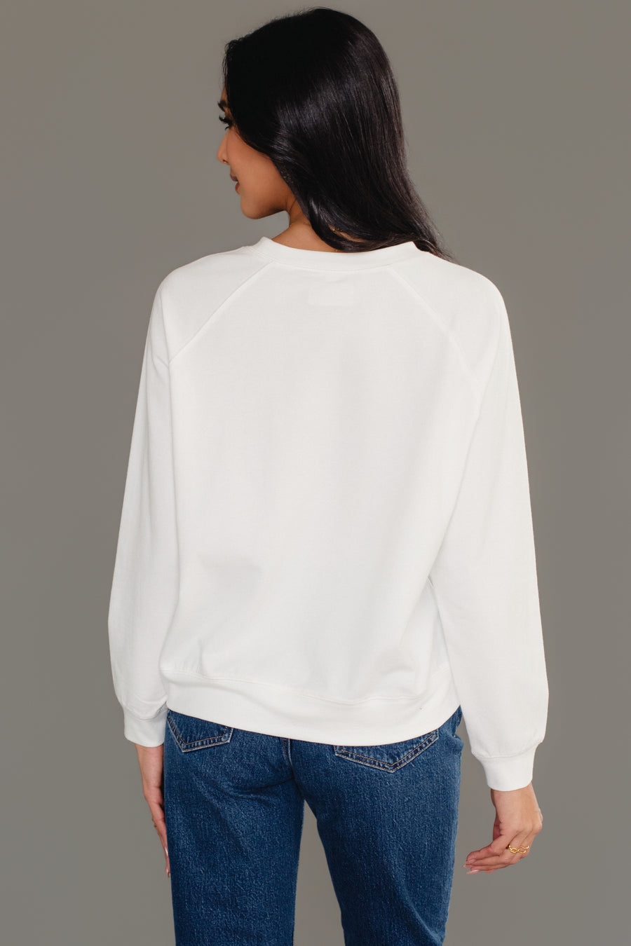 Back view of a person wearing a plain white long-sleeved Christmas Girl & Dog Sweatshirt and blue jeans.