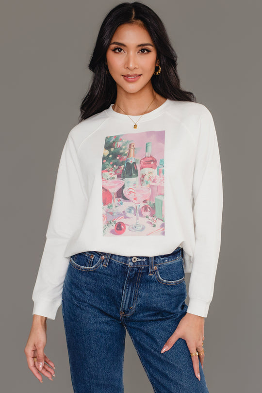 A woman wearing a white Panache Apparel Collection Christmas Cocktails Scene Sweatshirt featuring a graphic print of Christmas cocktails, a bottle of champagne, and wrapped gifts.