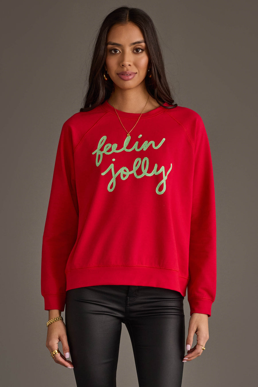 A person wearing an oversized red Feelin Jolly Sweatshirt by Panache Apparel Collection with the text embroidered in green script across the chest.