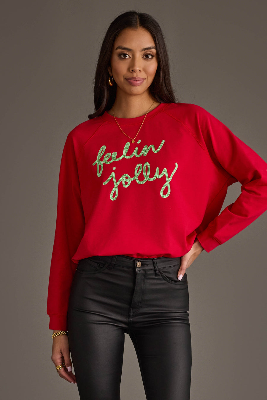 A person wears an oversized red Feelin Jolly Sweatshirt by Panache Apparel Collection with Feelin Jolly written in green cursive text across the chest.