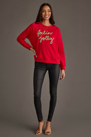 A woman wearing an oversized red Feelin Jolly Sweatshirt from the Panache Apparel Collection, paired with black skinny pants and tan heeled sandals.