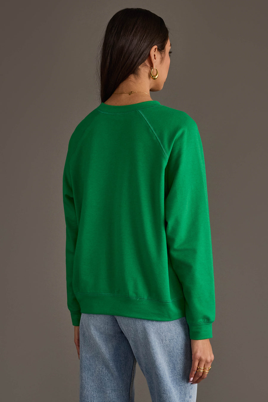 A person seen from behind wearing a green Jingle All The Way Sweatshirt by Panache Apparel Collection and light wash jeans.