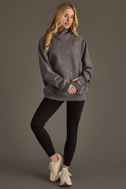 A woman with long blonde hair wears the Panache Apparel Collection’s “Dancing Skeletons” Hooded Sweatshirt, paired with black leggings and white sneakers, standing against a plain gray background.