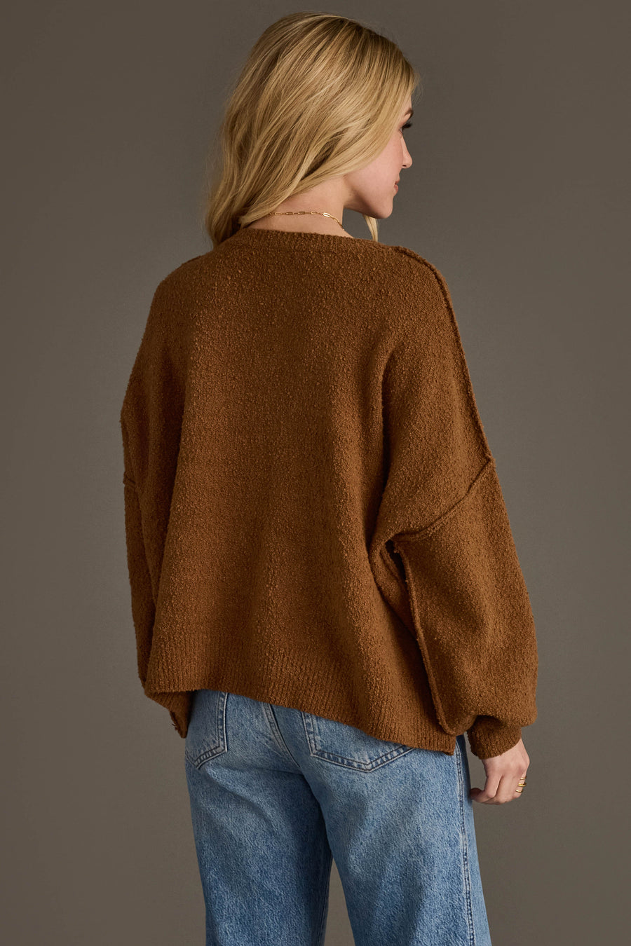 A person seen from behind wearing a Brown Gingerbread Sweater with exposed seams and blue jeans.