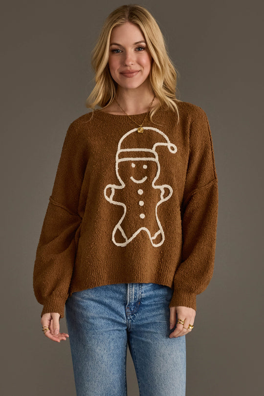 A woman wears a Brown Gingerbread Sweater featuring a large, white outline of a gingerbread person wearing a Santa hat.