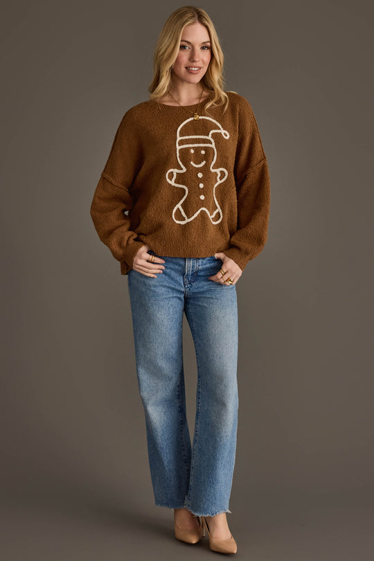 A person wearing a Brown Gingerbread Sweater featuring a white gingerbread man design and blue wide-leg jeans.