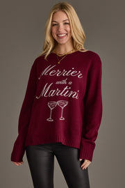 A smiling woman wearing a burgundy Panache Apparel Collection Merrier with a Martini Sweater featuring the text Merrier with a Martini above an illustration of two martini glasses.