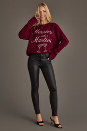 A smiling woman wears a burgundy Merrier with a Martini Sweater featuring a graphic of two martini glasses, paired with black skinny pants and black heeled sandals.