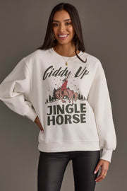 A smiling woman wears an off-white Panache Apparel Collection Giddy Up Jingle Horse Sweatshirt featuring a graphic of a person riding a horse and the text Giddy Up Jingle Horse.