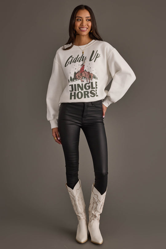A person wearing a Giddy Up Jingle Horse Sweatshirt featuring a cowboy on a horse, paired with black skinny pants and white cowboy boots.