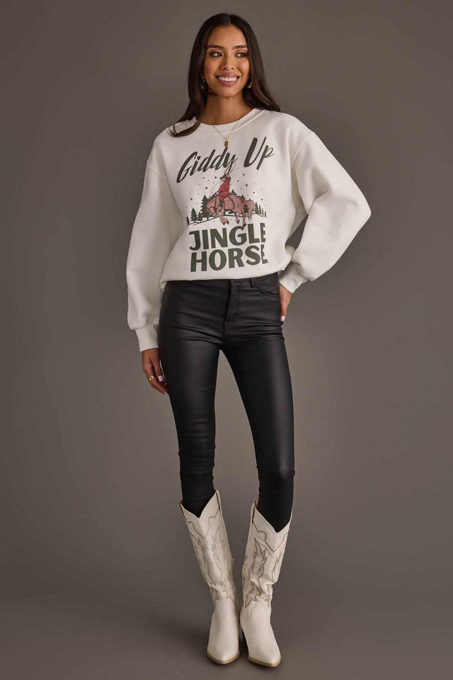 A person wearing a Giddy Up Jingle Horse Sweatshirt featuring a cowboy on a horse, paired with black skinny pants and white cowboy boots.