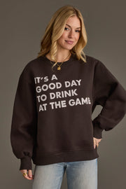 A blonde-haired woman poses against a plain gray background, wearing the Panache Apparel Collection It's A Good Day To Drink At The Game Sweatshirt and placing one hand on her hip.