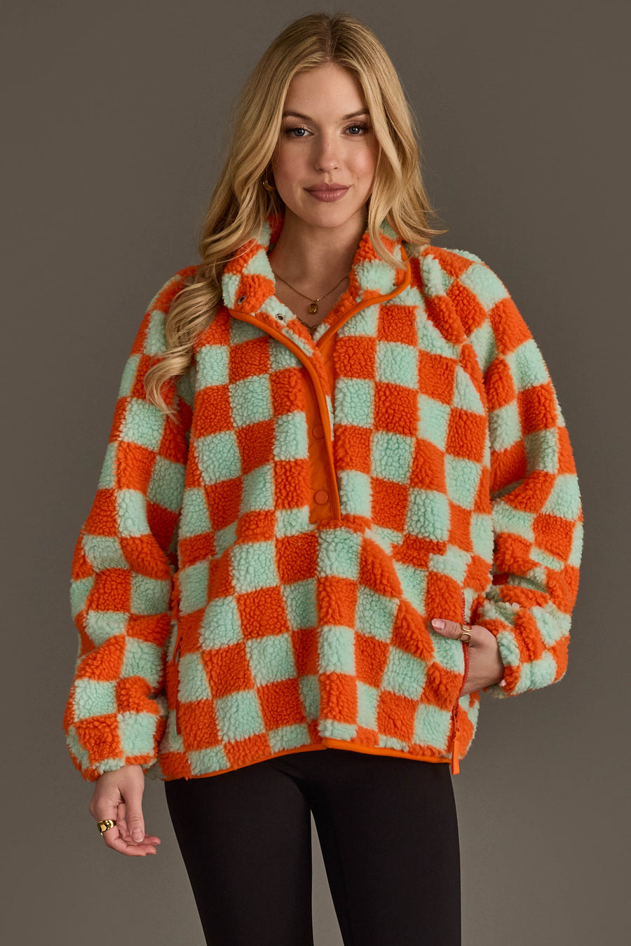 A woman models the Panache Apparel Collection Orange & Light Blue Checkered Fleece Sweatshirt against a plain background, casually placing one hand in her pocket and flashing a slight smile.