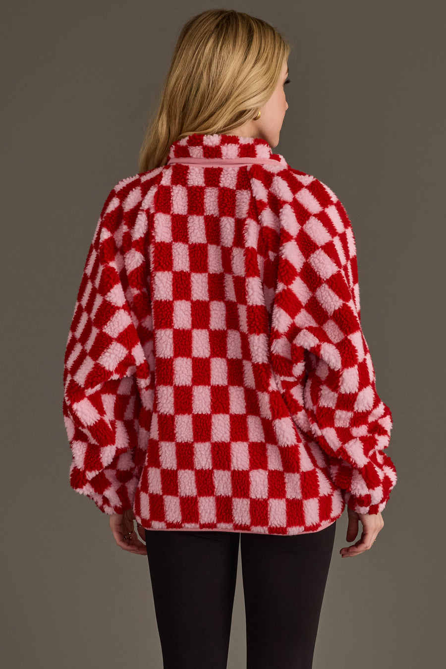 A person with long blonde hair is shown from behind against a plain brown background, wearing black pants and a Panache Apparel Collection Light Pink & Red Checkered Fleece Sweatshirt.