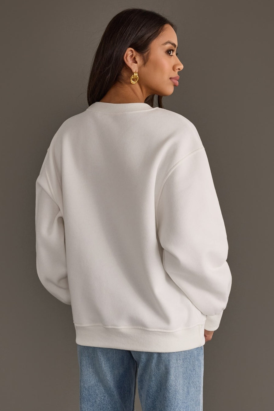 A woman seen from the back wearing a cozy, white oversized Feelin Festive Sweatshirt from Panache Apparel Collection and blue jeans.