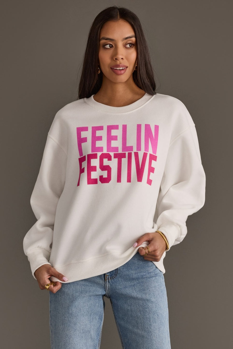 An oversized white Feelin Festive Sweatshirt featuring the words FEELIN FESTIVE in pink block lettering.