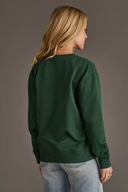 A person seen from the back wearing an oversized Dark Green Merry Sweatshirt and light-wash jeans.