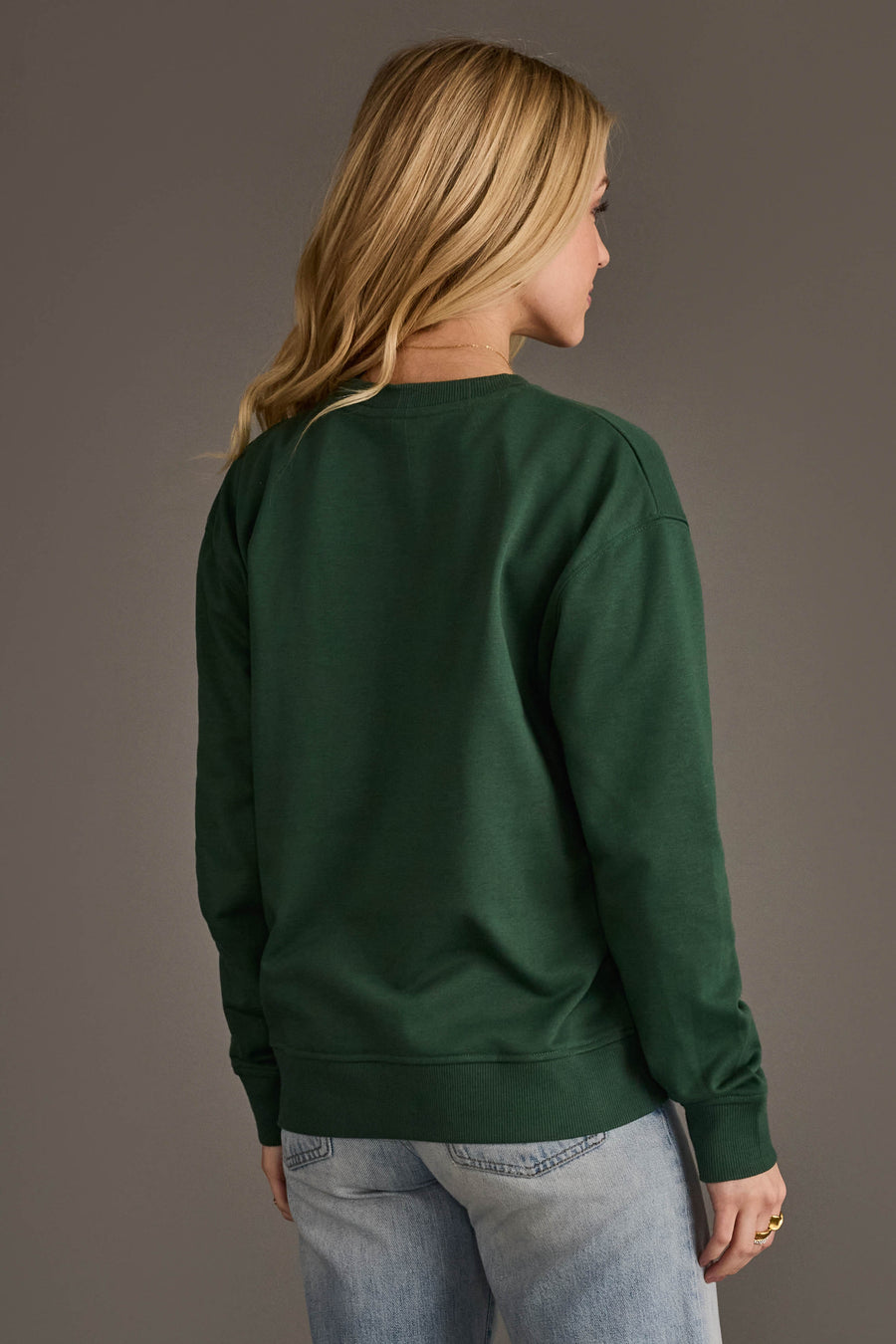 A person seen from the back wearing an oversized Dark Green Merry Sweatshirt and light-wash jeans.