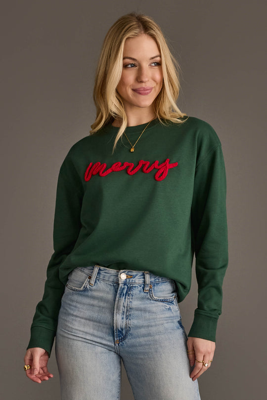 Woman wearing a dark green Dark Green Merry Sweatshirt with the word merry in red script embroidery on the chest.