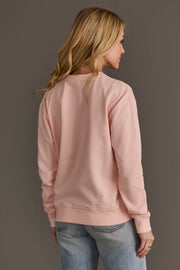 A woman viewed from the back wearing a Light Pink Merry Sweatshirt and blue jeans.