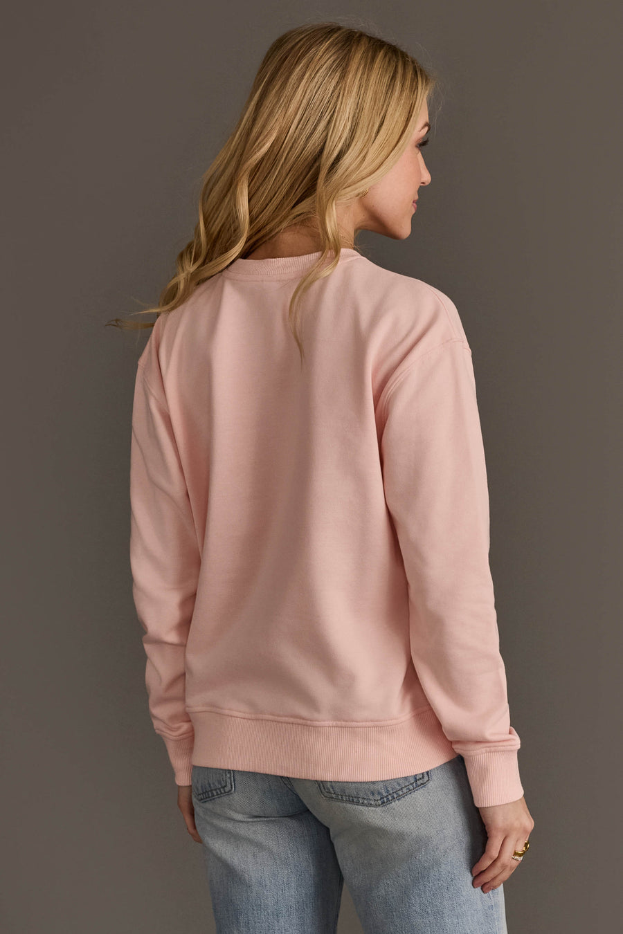 A woman viewed from the back wearing a Light Pink Merry Sweatshirt and blue jeans.